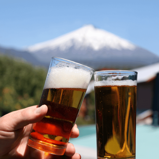 Personas brindando con cervezas frente a un volcán nevado en Pucón